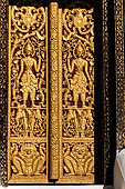 Wat Xieng Thong temple in Luang Prabang, Laos. Detail of a wooden door of the sim with gilded carvings on a red background. 